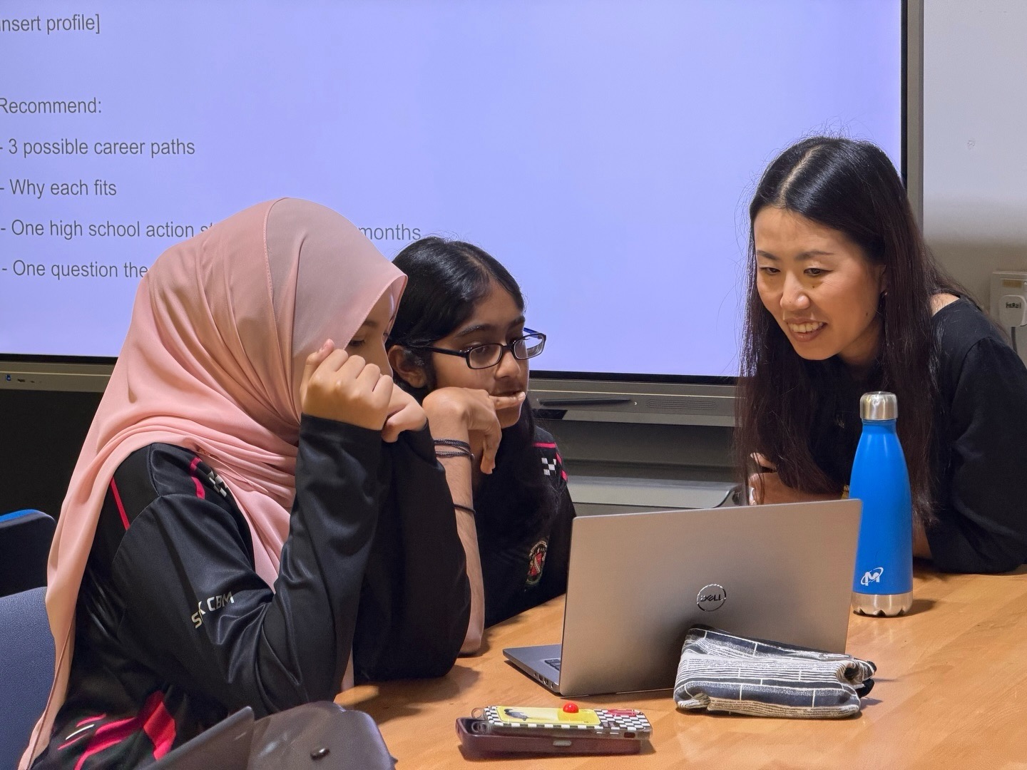 Lijie Zhou working one-on-one with two Penang Science Cluster students at a laptop during the AI-assisted career-exploration clinic, December 30, 2025