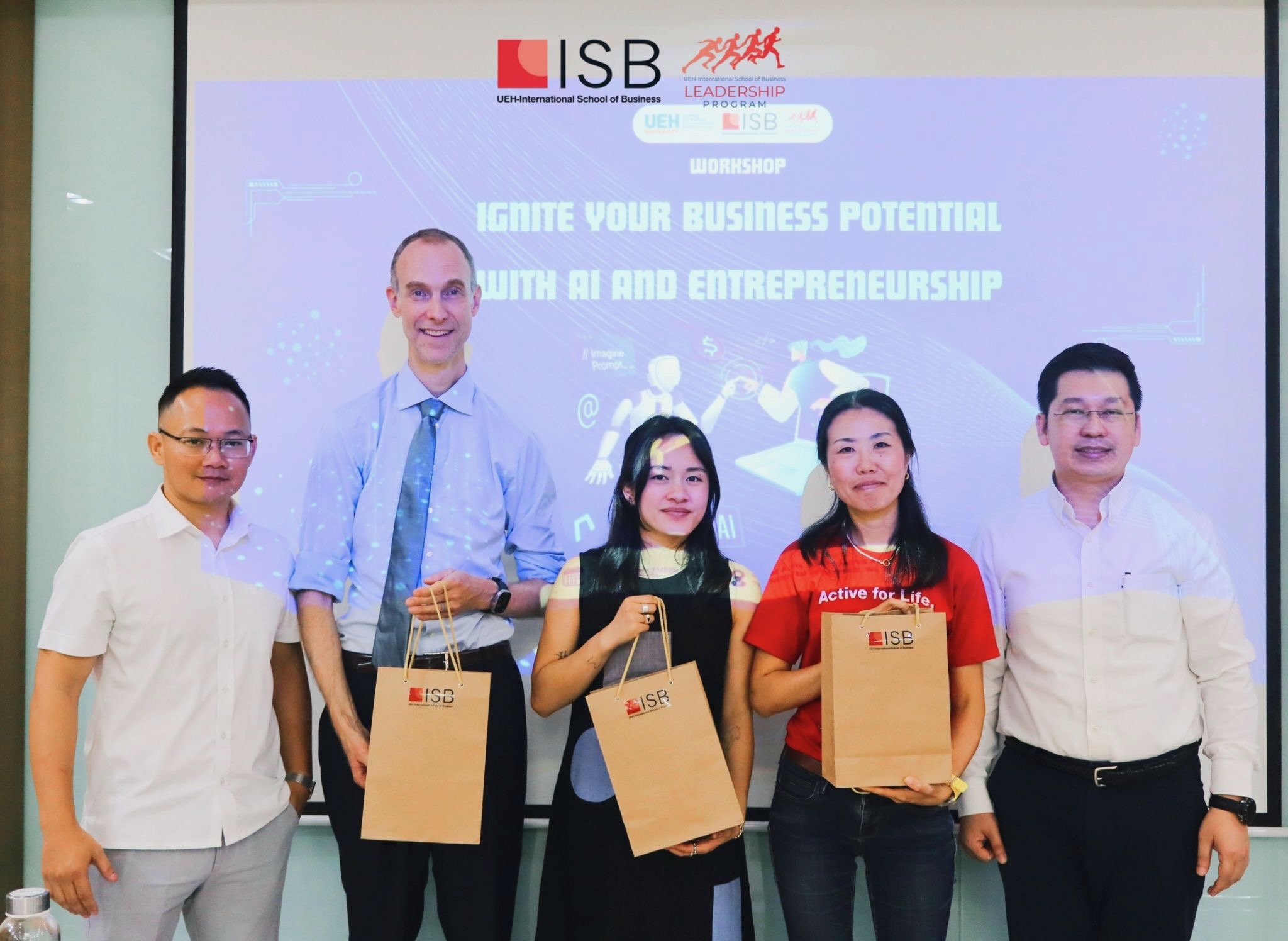 Chuck Eesley, Lijie Zhou, and three UEH ISB organizers holding ISB gift bags in front of the Ignite Your Business Potential with AI and Entrepreneurship title slide at the close of the workshop