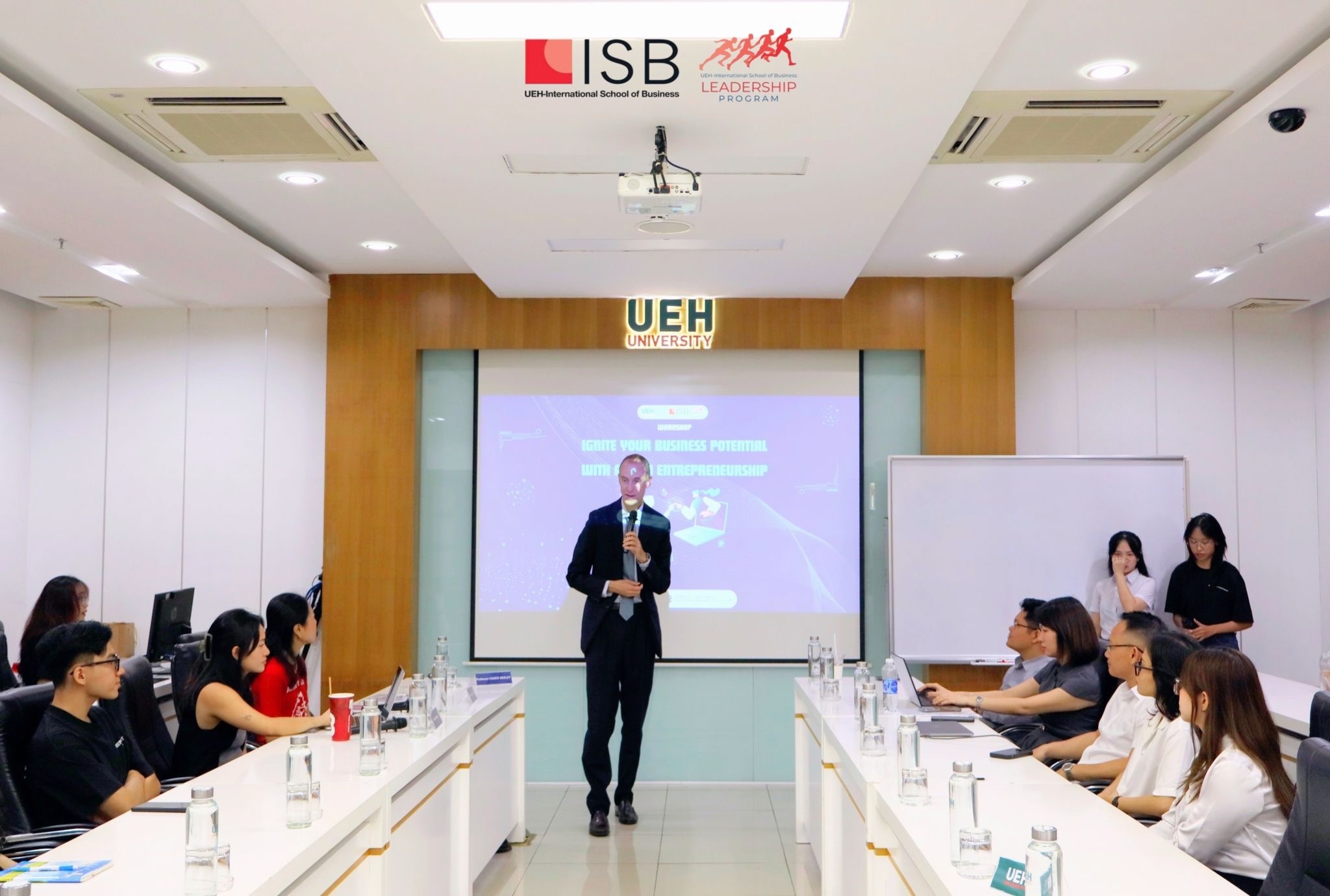 Chuck Eesley at the front of a UEH ISB classroom with the Ignite Your Business Potential with AI and Entrepreneurship workshop title slide projected behind him and students seated at conference tables on either side